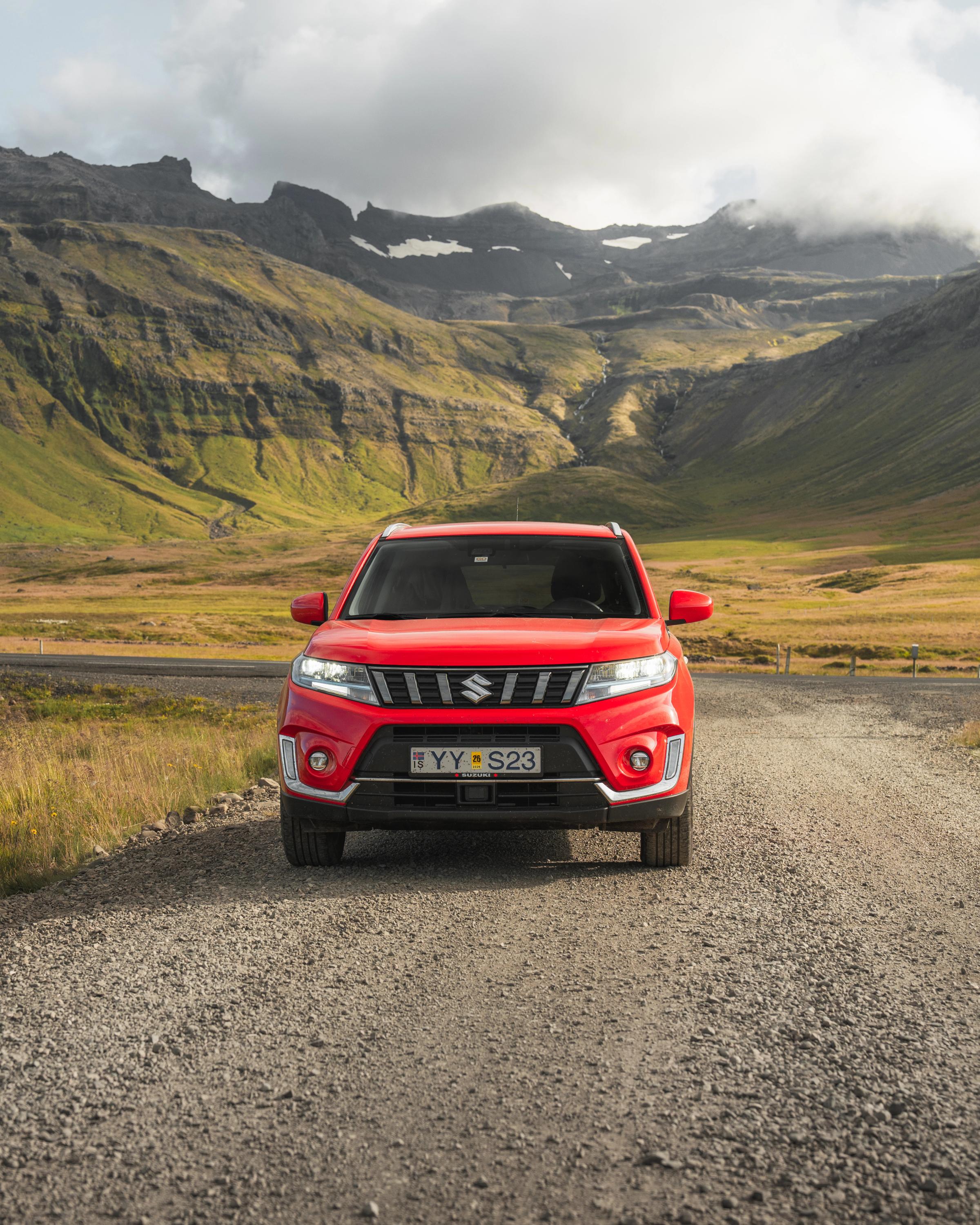 Vue de face d’un SUV Suzuki Vitara sur une route de gravier, avec un paysage montagneux en arrière-plan