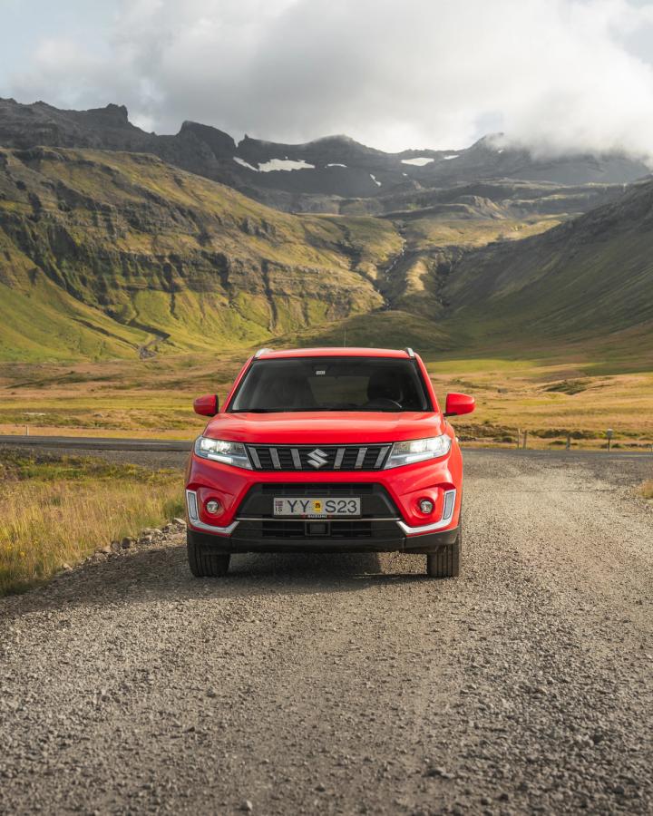Vue de face d’un SUV Suzuki Vitara sur une route de gravier, avec un paysage montagneux en arrière-plan
