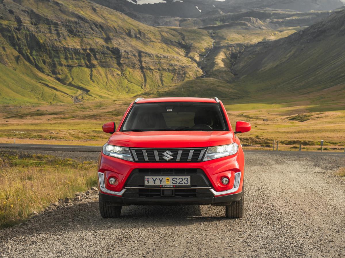 Vue avant du Vitara dans les Highlands Vue de face d’un SUV Suzuki Vitara sur une route de gravier, avec un paysage montagneux en arrière-plan