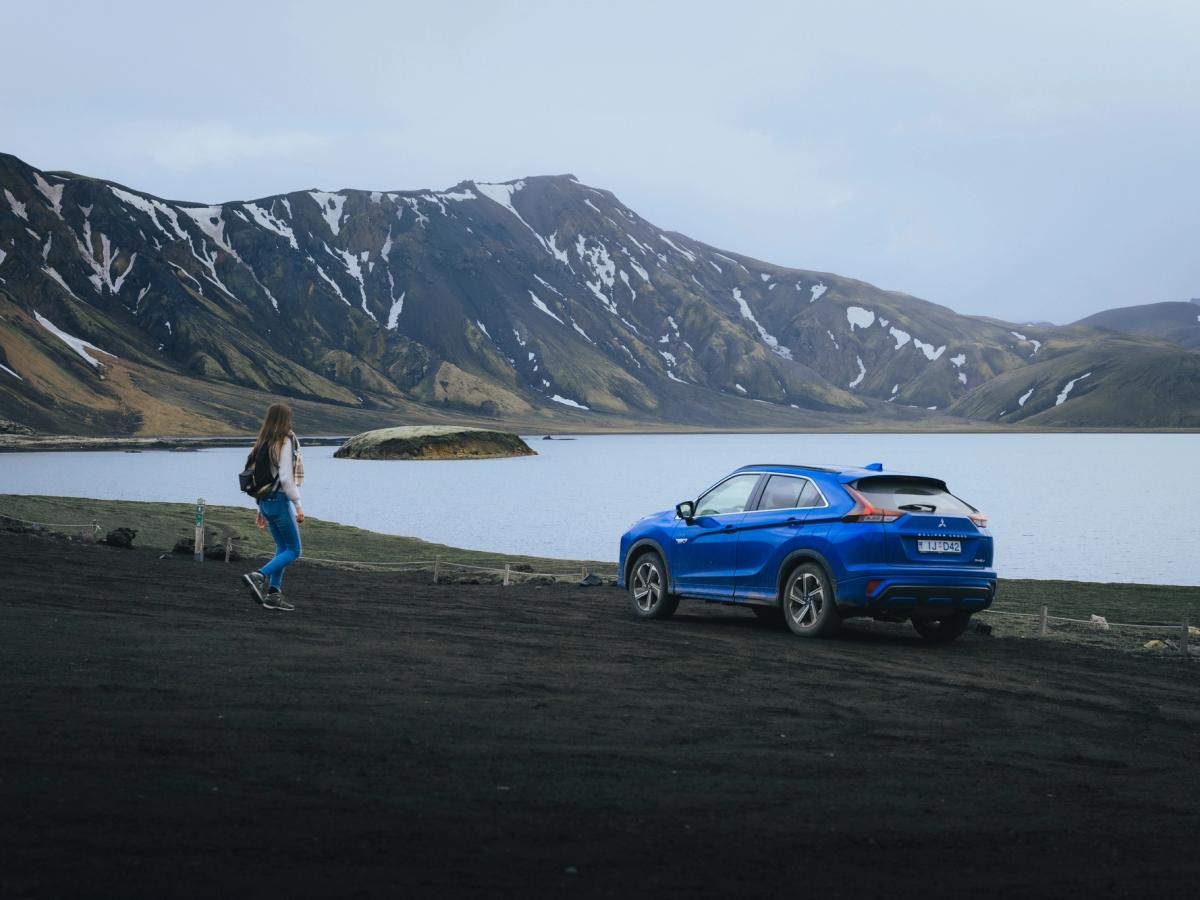 Mitsubishi Eclipse Cross Lake View Mitsubishi Eclipse Cross aparcado cerca de un lago, con montañas al fondo y una persona caminando por los alrededores