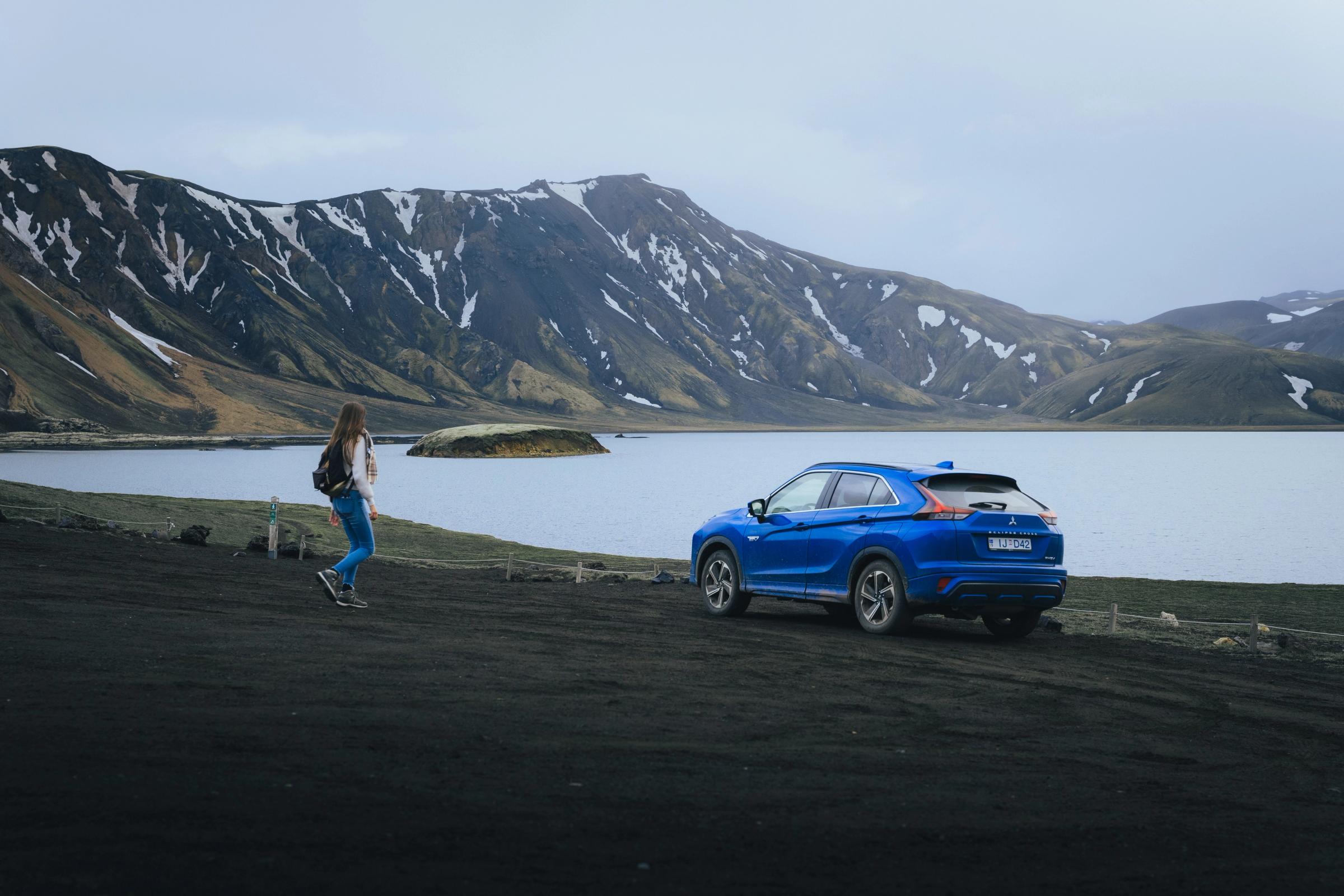Mitsubishi Eclipse Cross Lake View Mitsubishi Eclipse Cross aparcado cerca de un lago, con montañas al fondo y una persona caminando por los alrededores