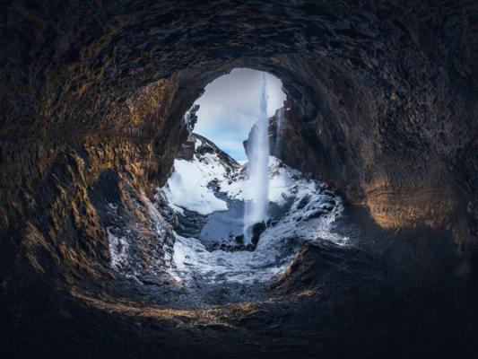 a waterfall is coming out of a cave in the mountains at Kvernufoss in Iceland.