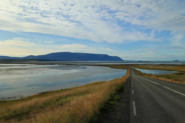 a road going through a lake with mountains in the background,  Golden Circle Road