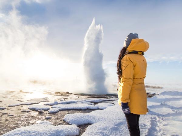Chica vestida con un abrigo amarillo admirando el Gran Geyser en Islandia