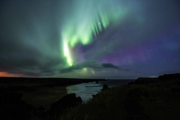 the aurora borealis is dancing in the night sky over a body of water .