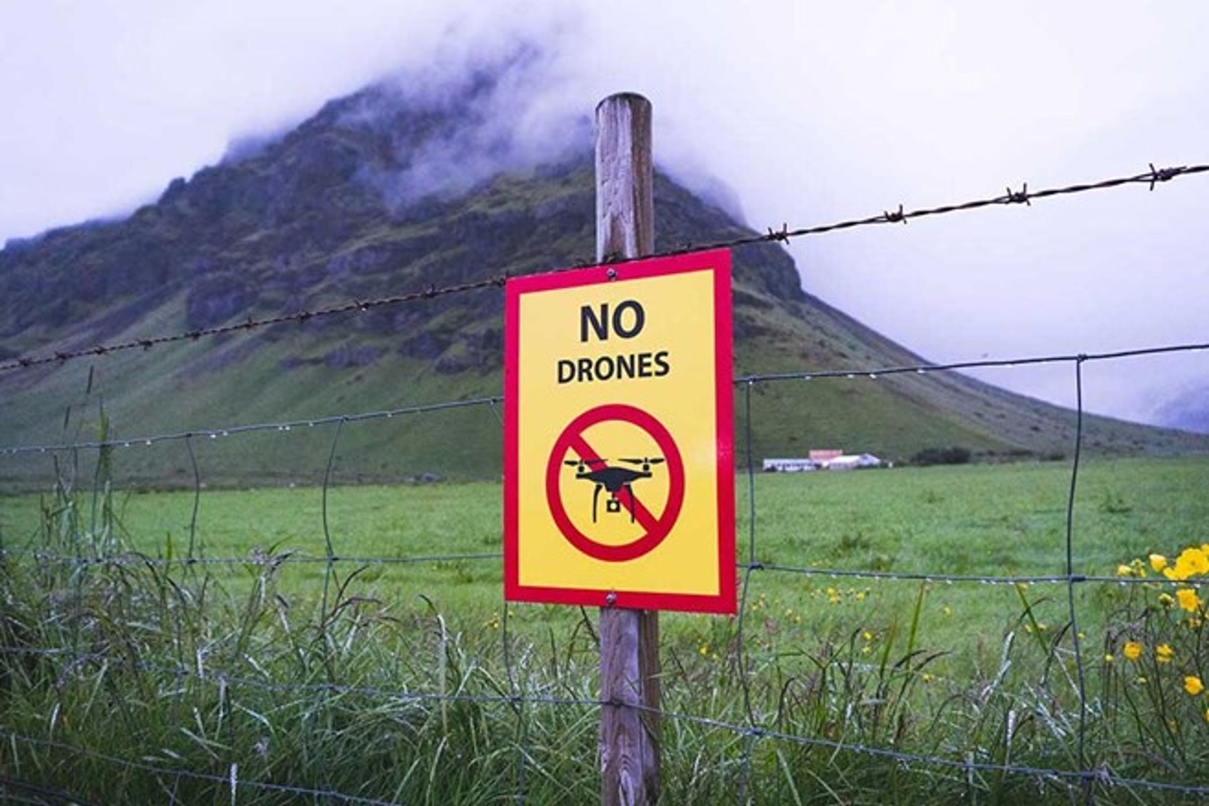 Un cartel con el mensaje "prohibido el uso de drones" en una valla con una montaña de fondo
