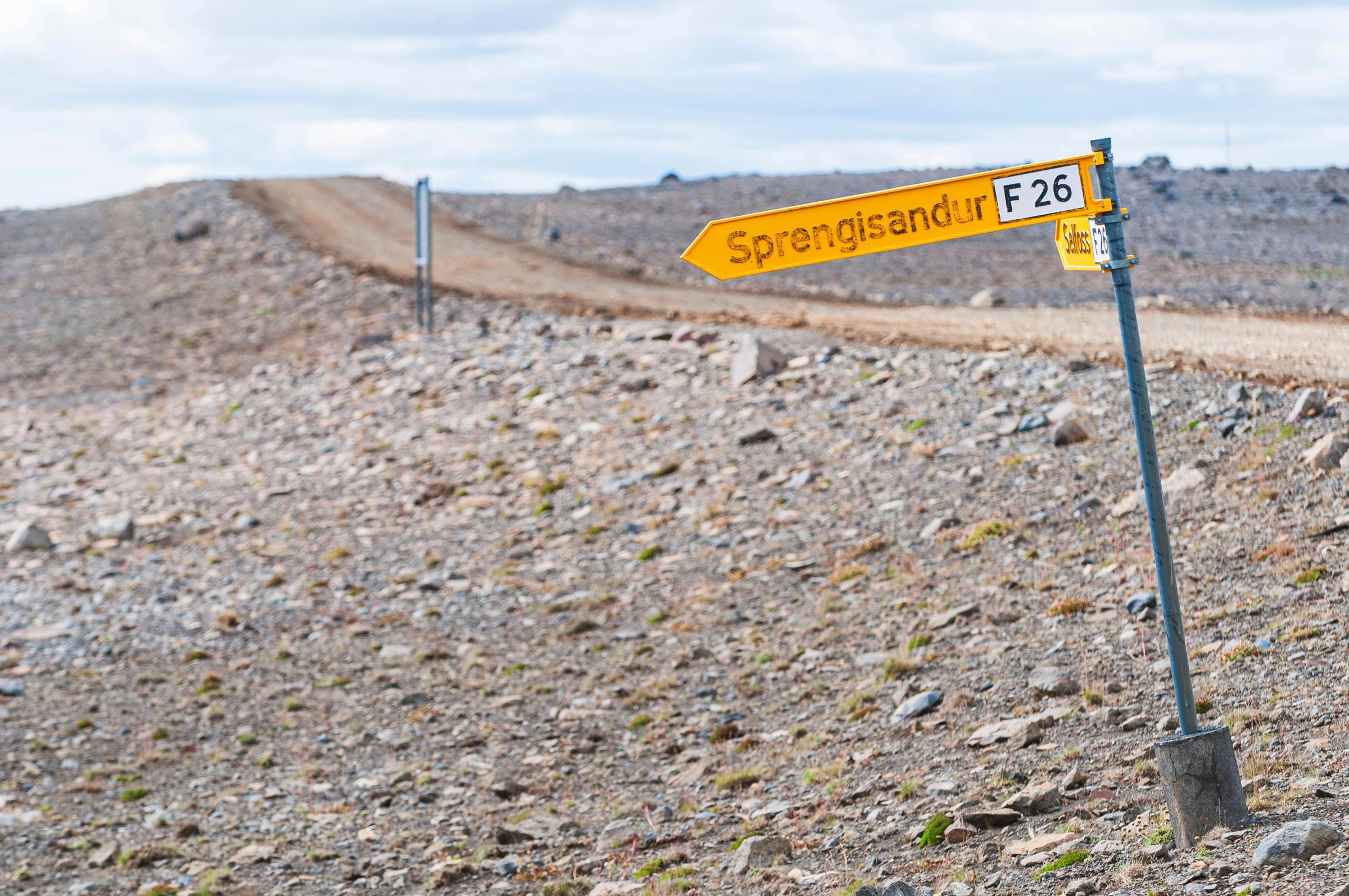 a yellow sign on the side of a dirt road .