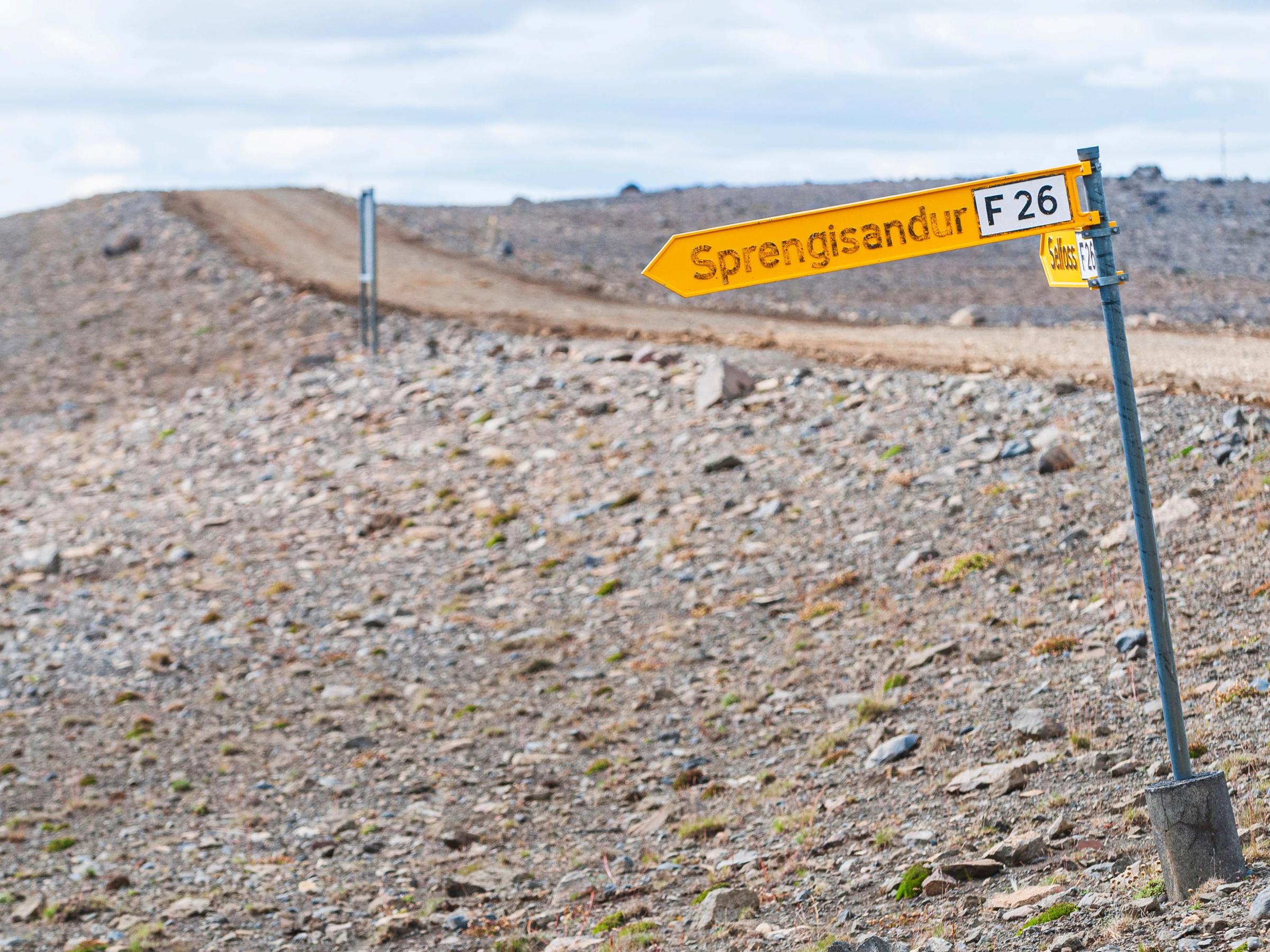 a yellow sign on the side of a dirt road .