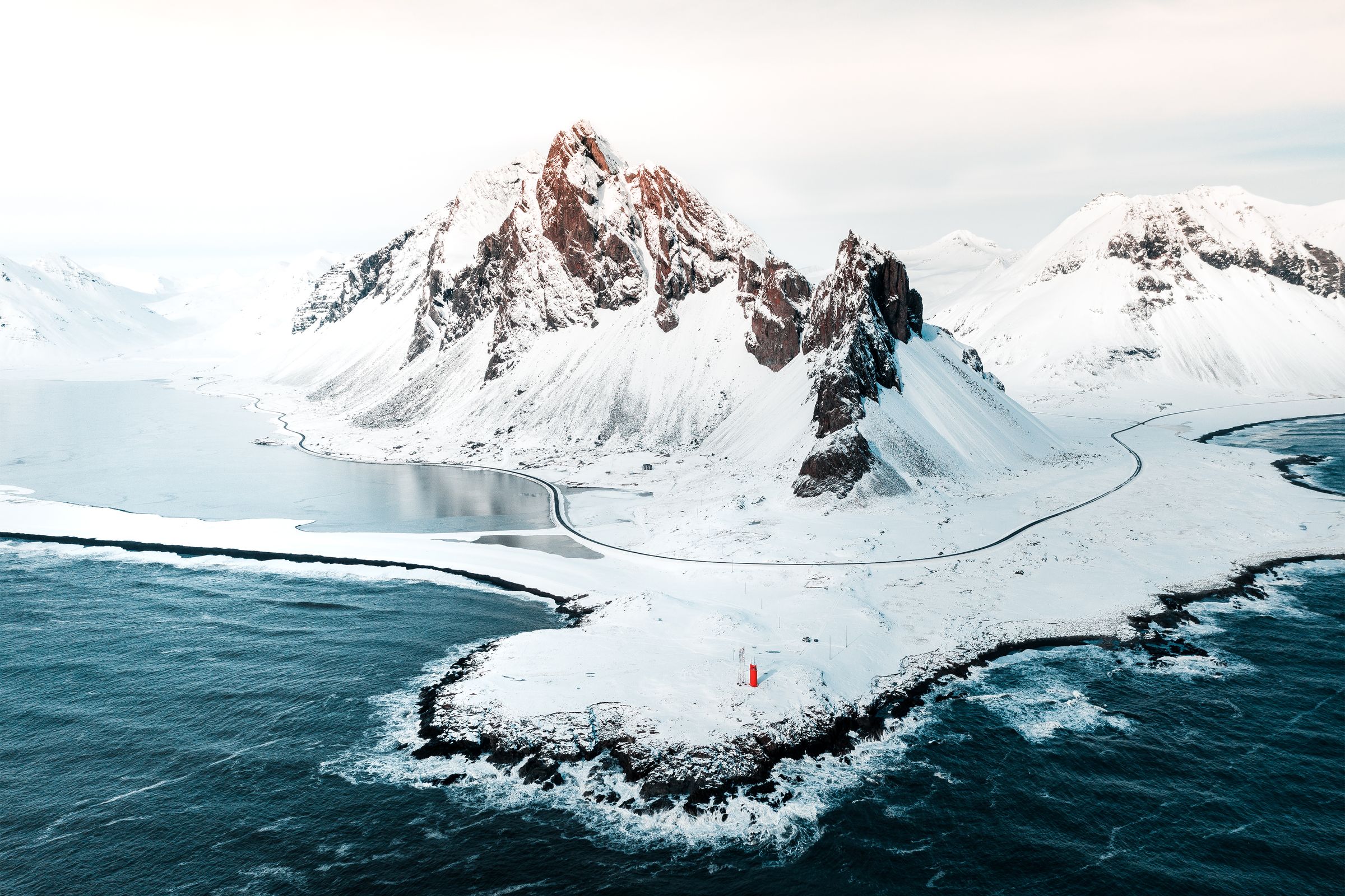 a snowy landscape of a mountain next to the sea