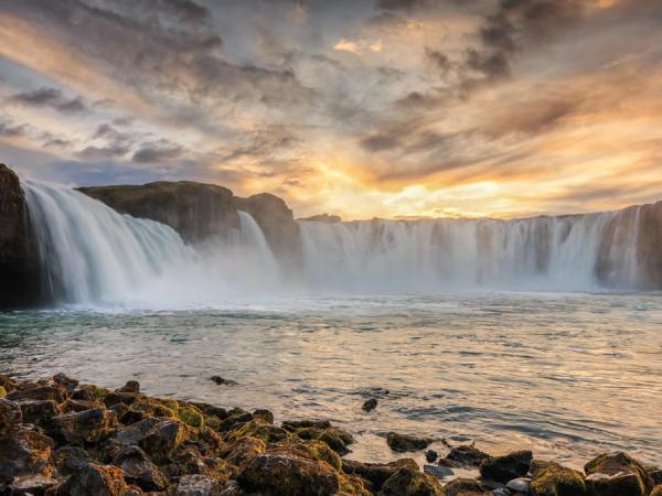 una cascada está rodeada de rocas y agua al atardecer.
