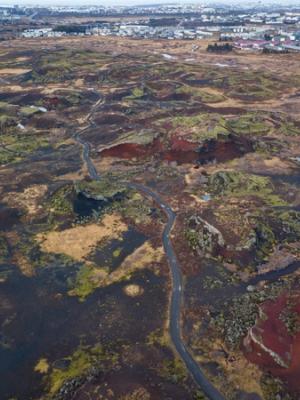 an aerial view of a road going through a lush green field .