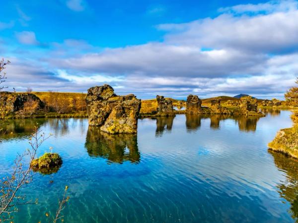 a large body of water surrounded by rocks and trees on a sunny day at lake myvatn in north iceland.