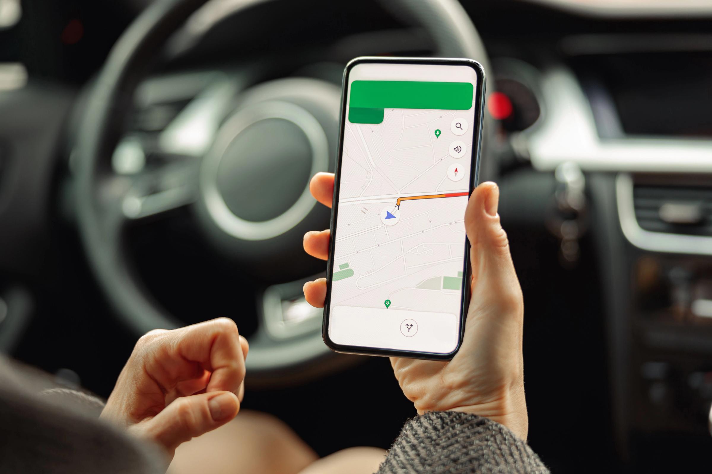 Close-up image of a woman in a rental car in Iceland, using her cell phone with a GPS navigation app on screen.