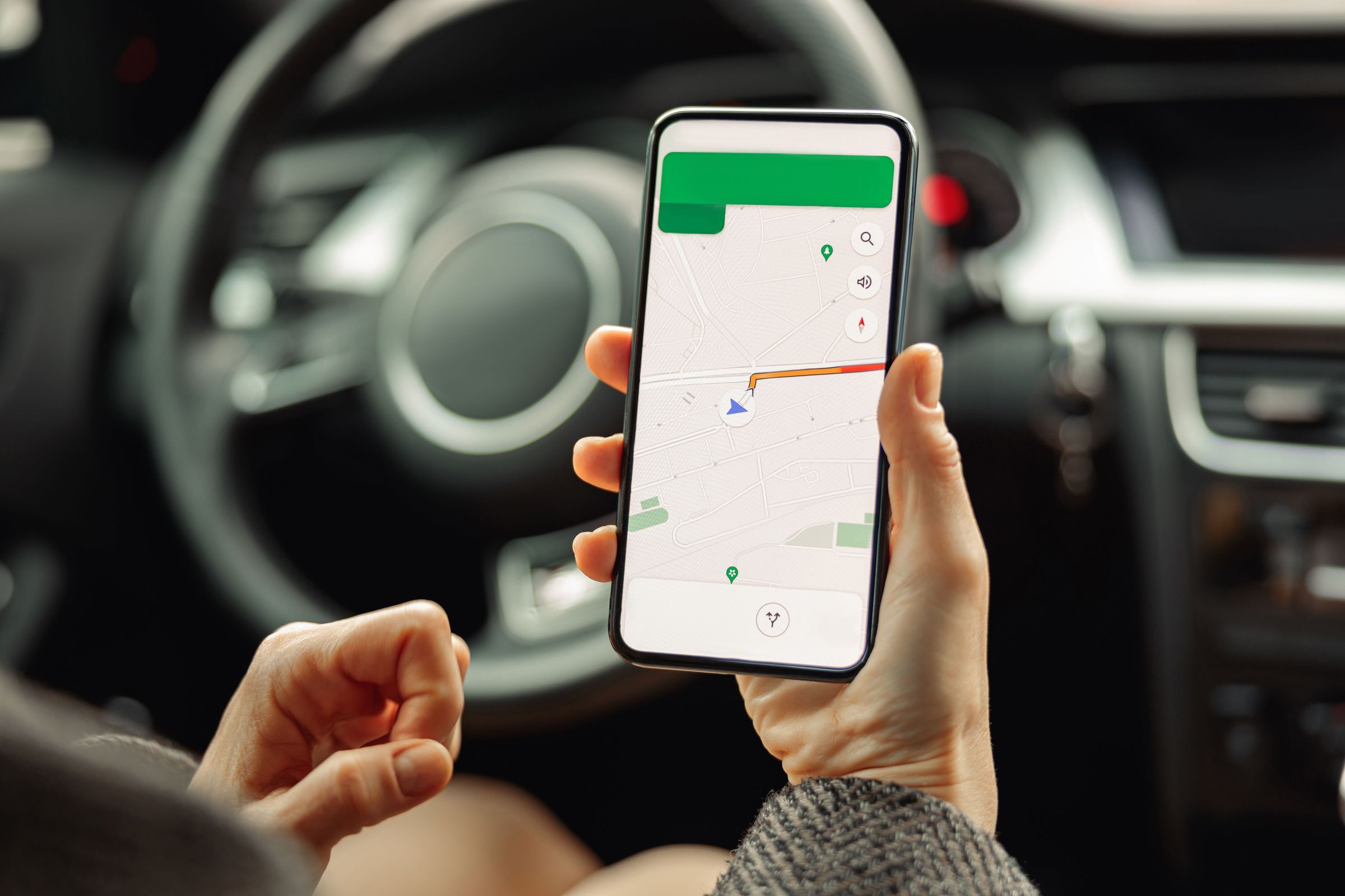 Navigating Iceland's vast terrains with GPS: The modern traveler's compass. Close-up image of a woman in a rental car in Iceland, using her cell phone with a GPS navigation app on screen.
