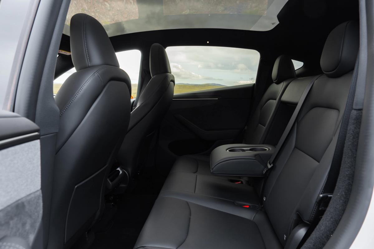 Asientos traseros del Tesla Model Y con reposabrazos central y portavasos, espacioso coche eléctrico de alquiler en Islandia