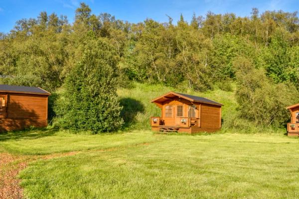 three wooden cabins are sitting on top of a lush green hillside in Hallormsstaðaskógur