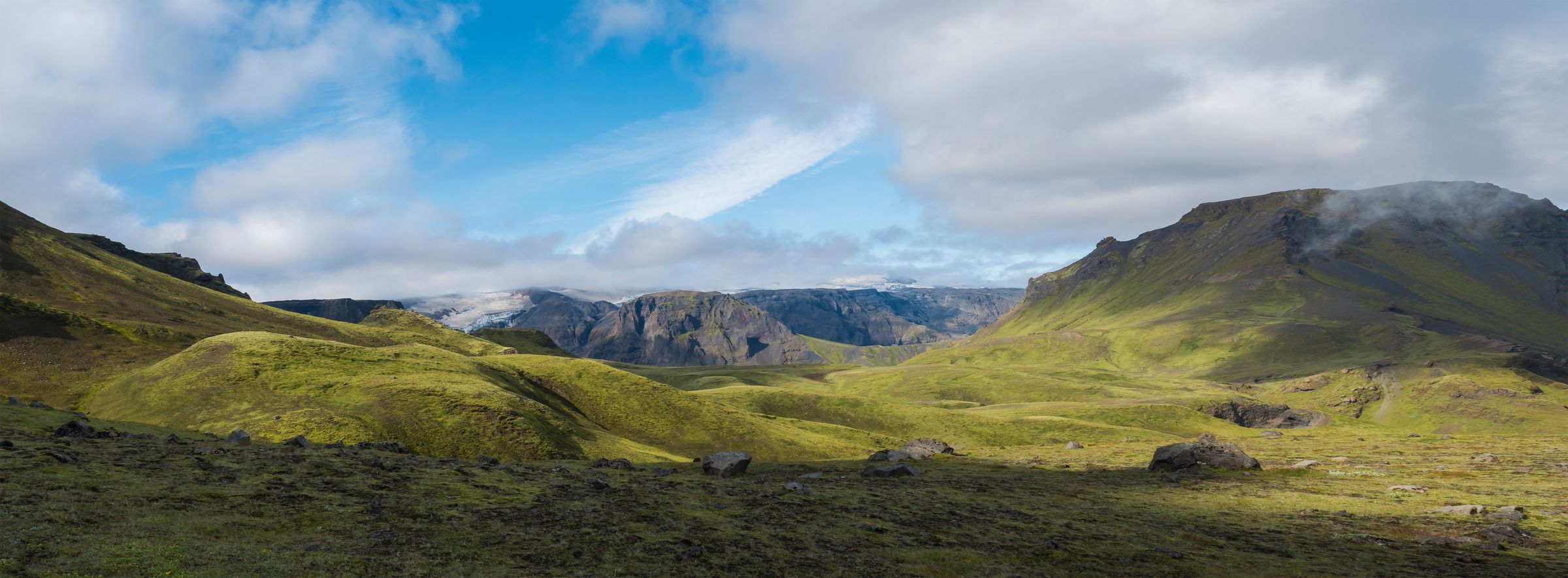 a panoramic view of a lush green valley with mountains in the background, Fimmvörðuháls