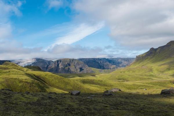 a panoramic view of a lush green valley with mountains in the background, Fimmvörðuháls