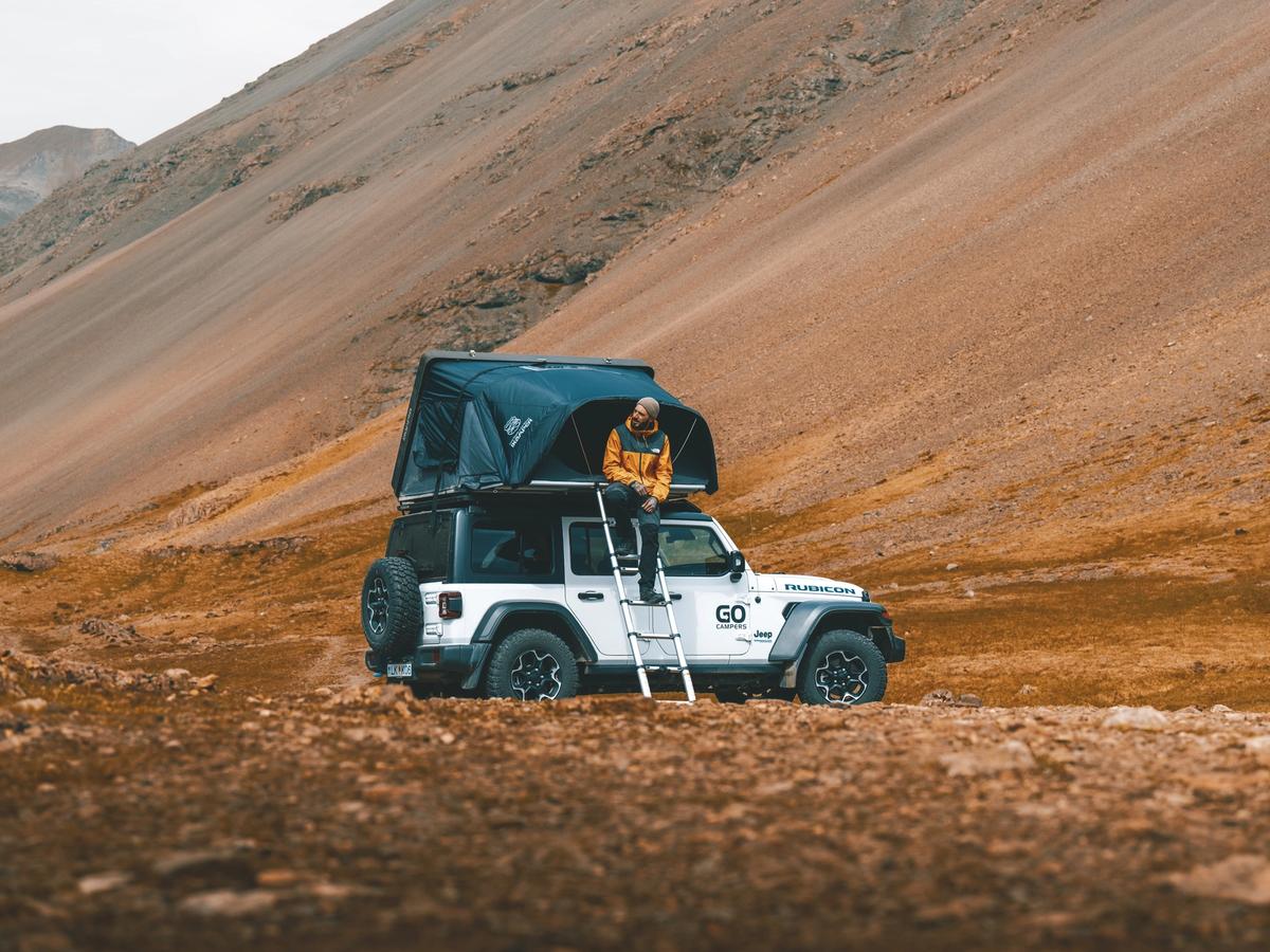 4x4 húsbíll í skriðu Fjögurra manna fjórhjóladrifinn húsbíll með opnu þaktjaldi undir bröttum skriðuhlíðum, húsbílaleiga á Íslandi