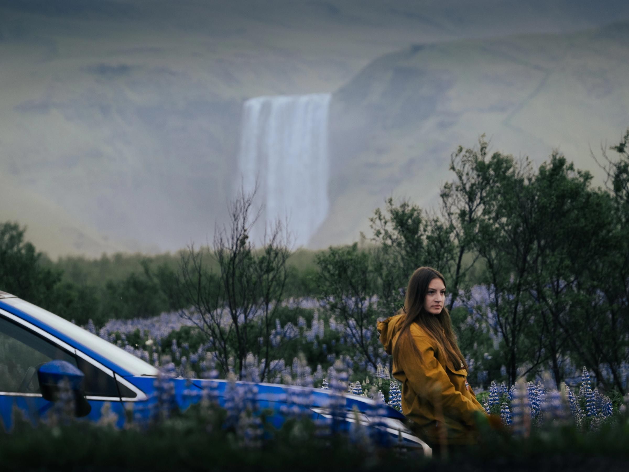 Mitsubishi Eclipse Cross en una escena con una cascada Silueta del techo de un Mitsubishi Eclipse Cross junto a una cascada y un campo de flores, con una persona sentada