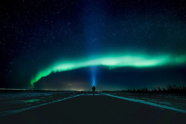 a person is standing on a road looking at the aurora borealis in iceland.