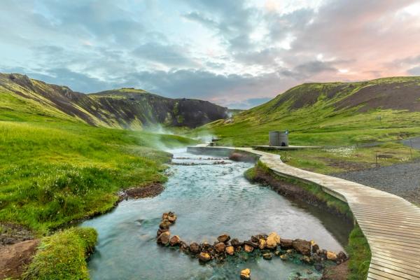 une passerelle en bois menant à une rivière au milieu d'un champ verdoyant aux sources chaudes de Reykjadalur en Islande.