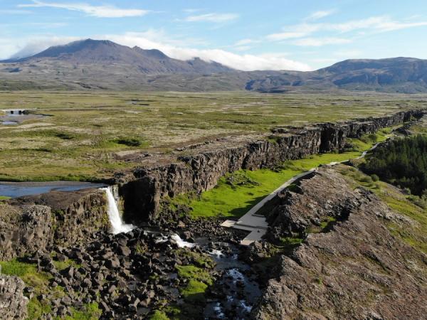 an aerial view of a waterfall in the middle of a field with mountains in the background .