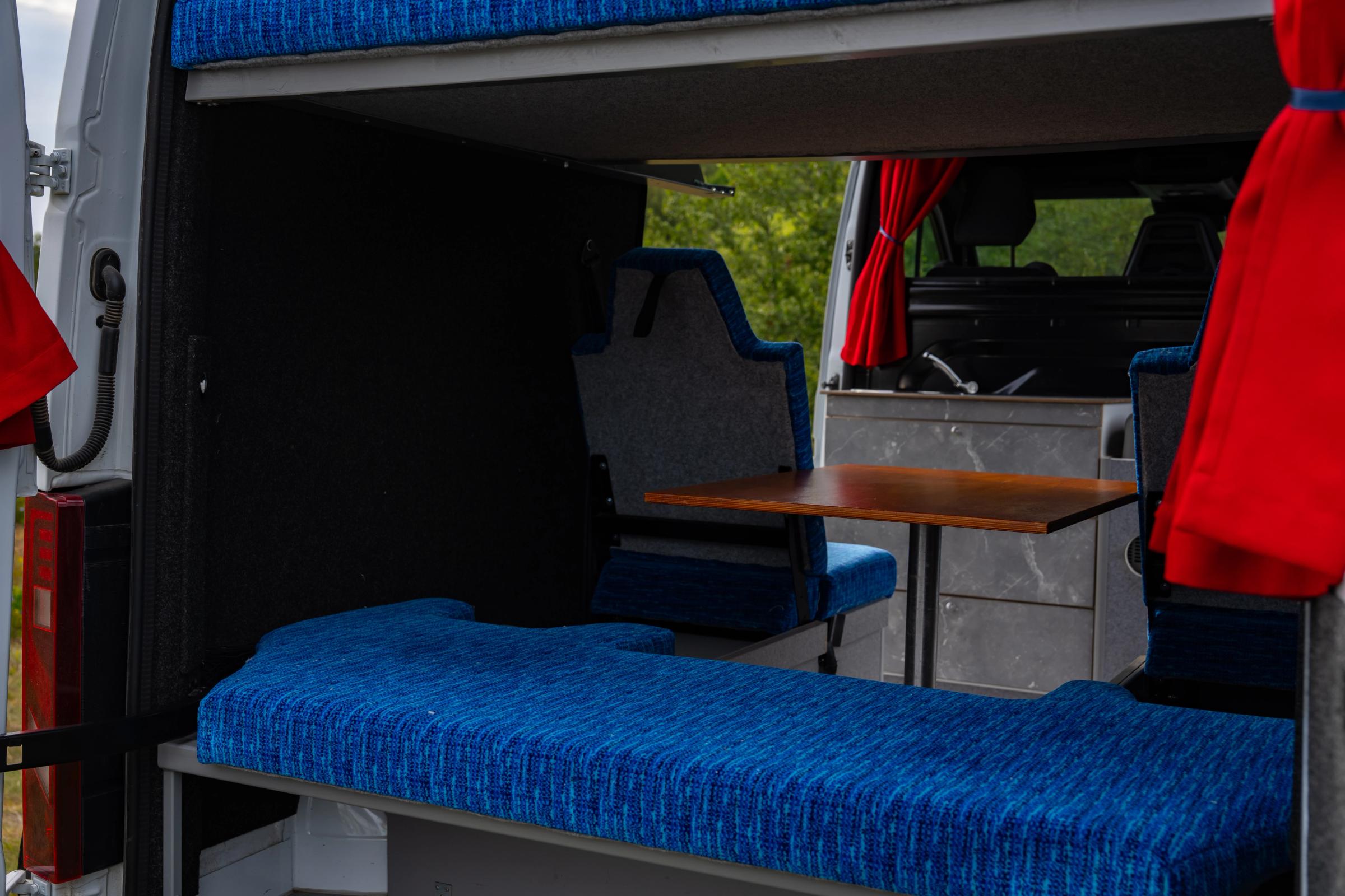 View through the rear doors of a blue bench seat, table and kitchen unit with sink