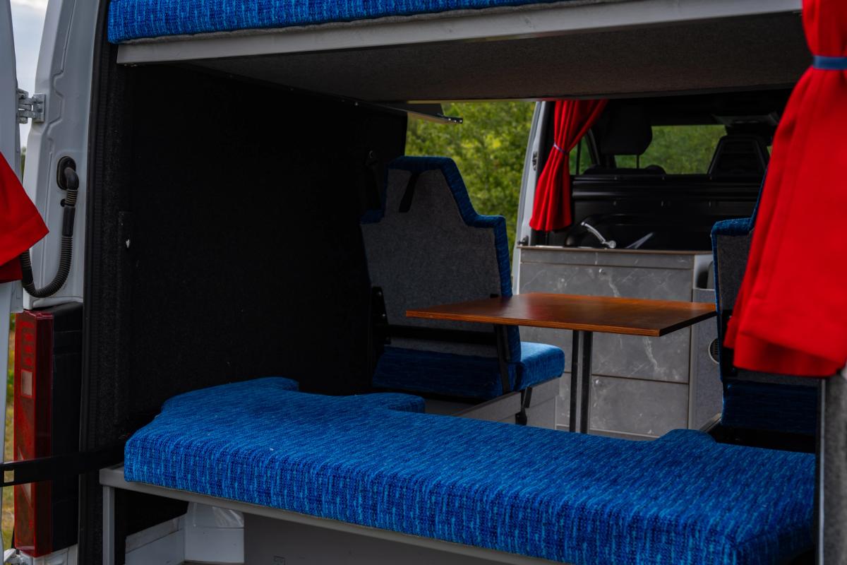 View through the rear doors of a blue bench seat, table and kitchen unit with sink