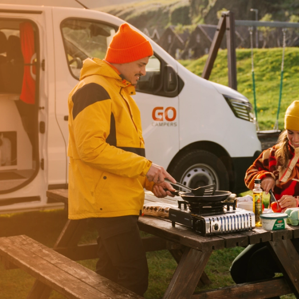 Pareja haciendo un picnic en una mesa de madera al lado de una cámper de Go Campers