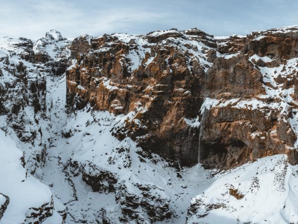 a waterfall is coming down the side of a snow covered mountain .