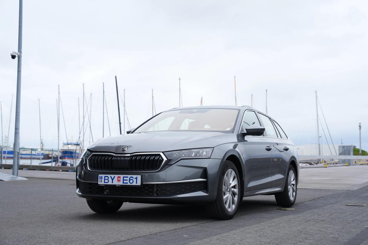 Skoda Octavia-stationbíll séður á ská að framan, lagt við höfn með seglbáta í bakgrunni