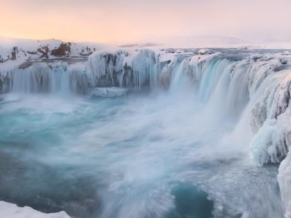 Una amplia cascada con agua de un azul vibrante rodeada de nieve pesada y carámbanos.