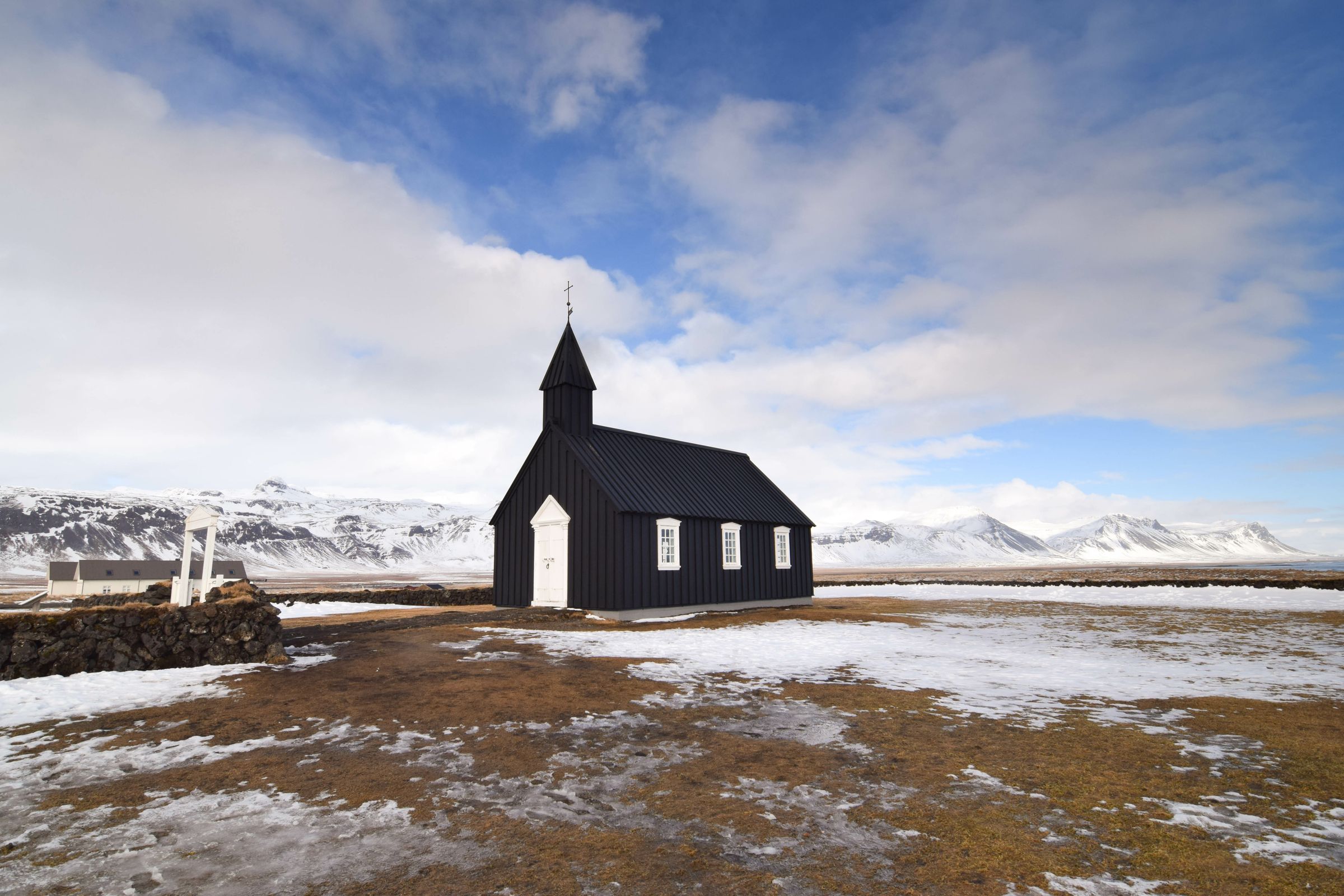 iglesia de madera negra en un campo con montañas nevadas al fondo