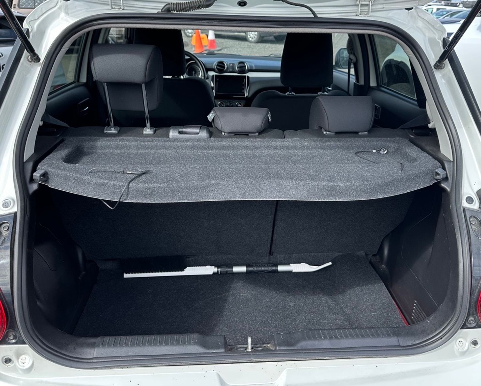 Empty trunk of a white hatchback with a grey cargo cover and a snow brush.
