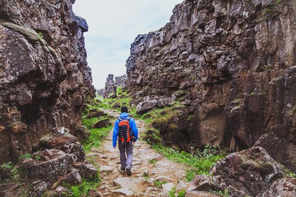Man with a blue coat and a red backpack hiking through a rocky path