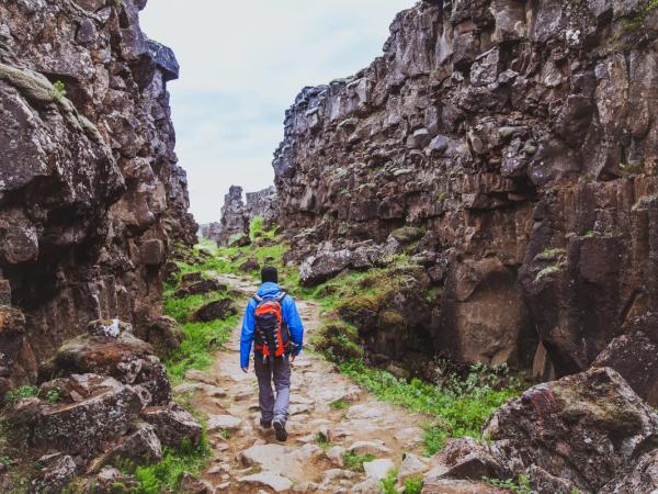 A person with a backpack walks on a rocky path between towering rock walls.
