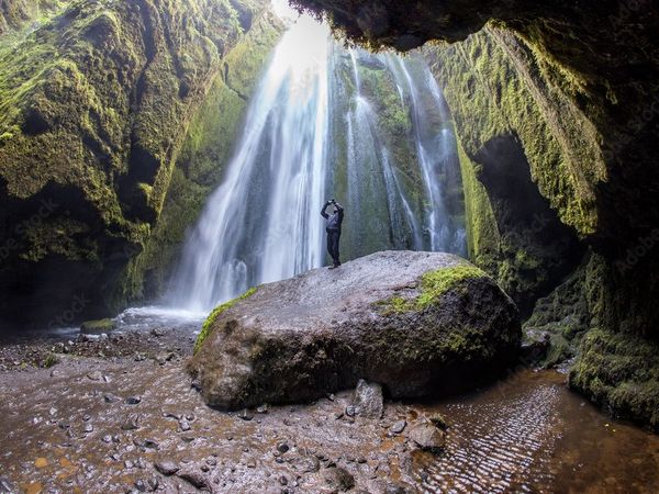 a man is standing on a rock in front of a waterfall in a cave .