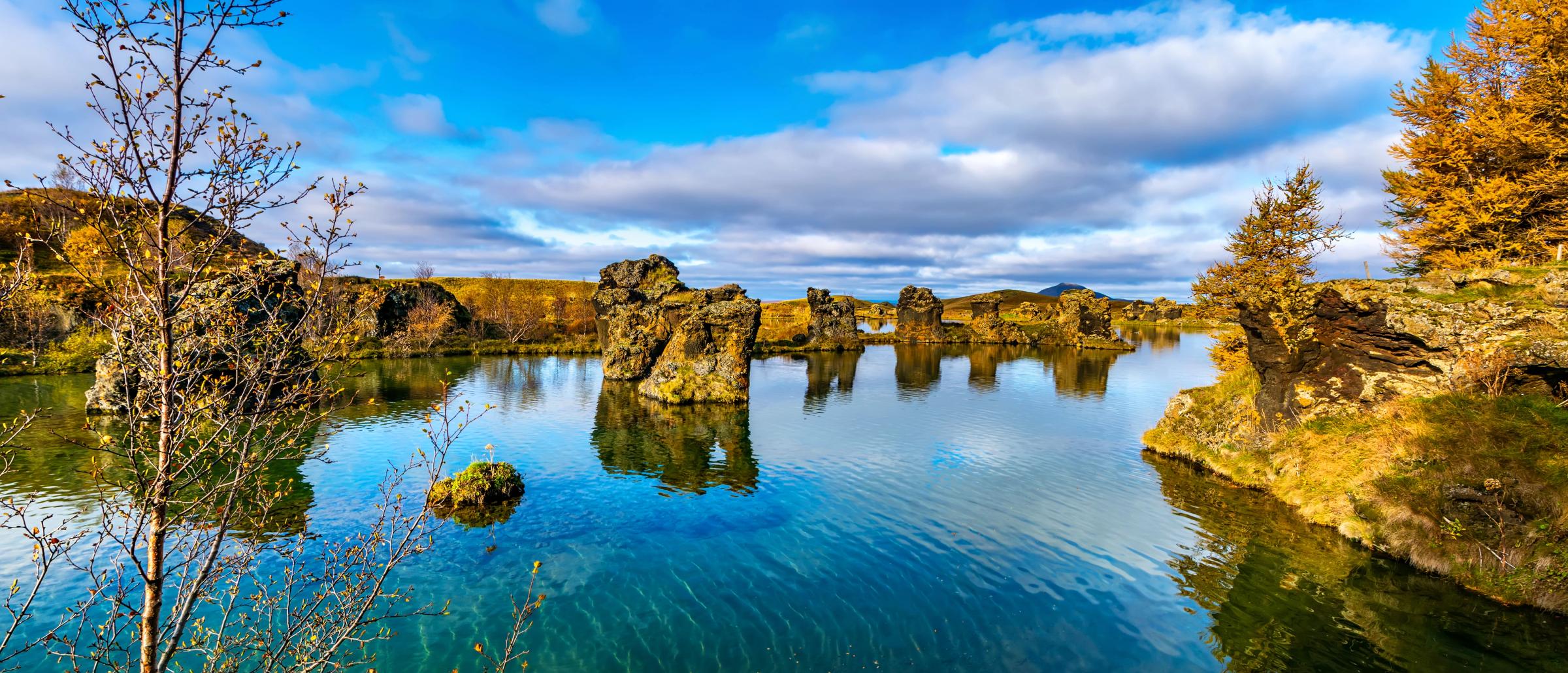 Un lago azul salpicado de formaciones rocosas escarpadas, rodeado de árboles otoñales bajo un cielo nublado.