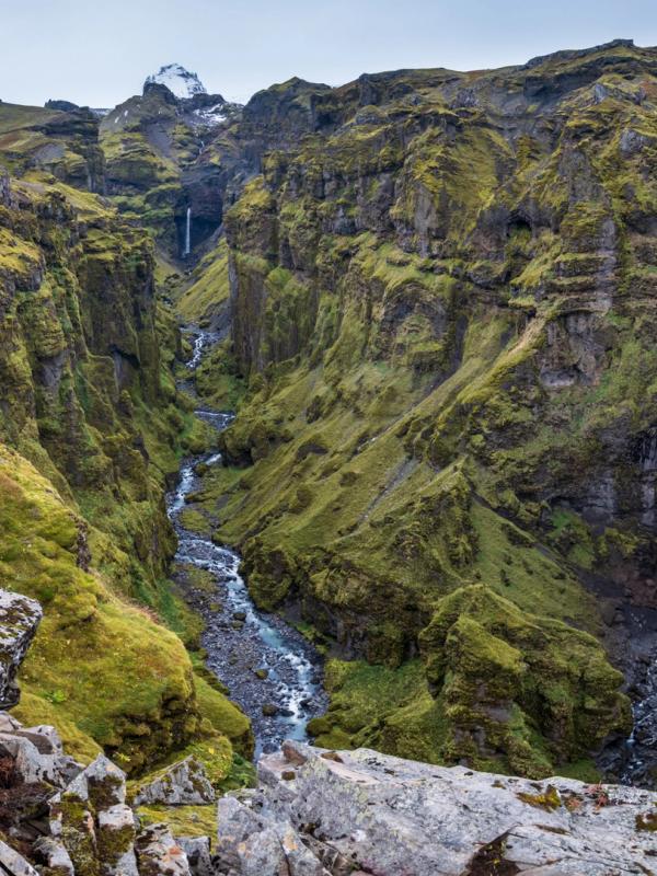 there is a waterfall in the middle of a canyon in the mountains .
