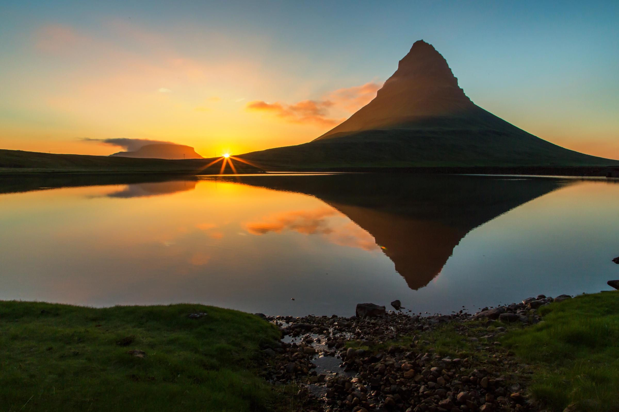 Atardecer dorado sobre la montaña Kirkjufell, reflejado a la perfección en un lago en calma.