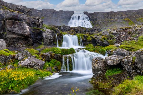 a waterfall is surrounded by rocks and grass in the middle of a mountain at Dynjandi in Iceland.