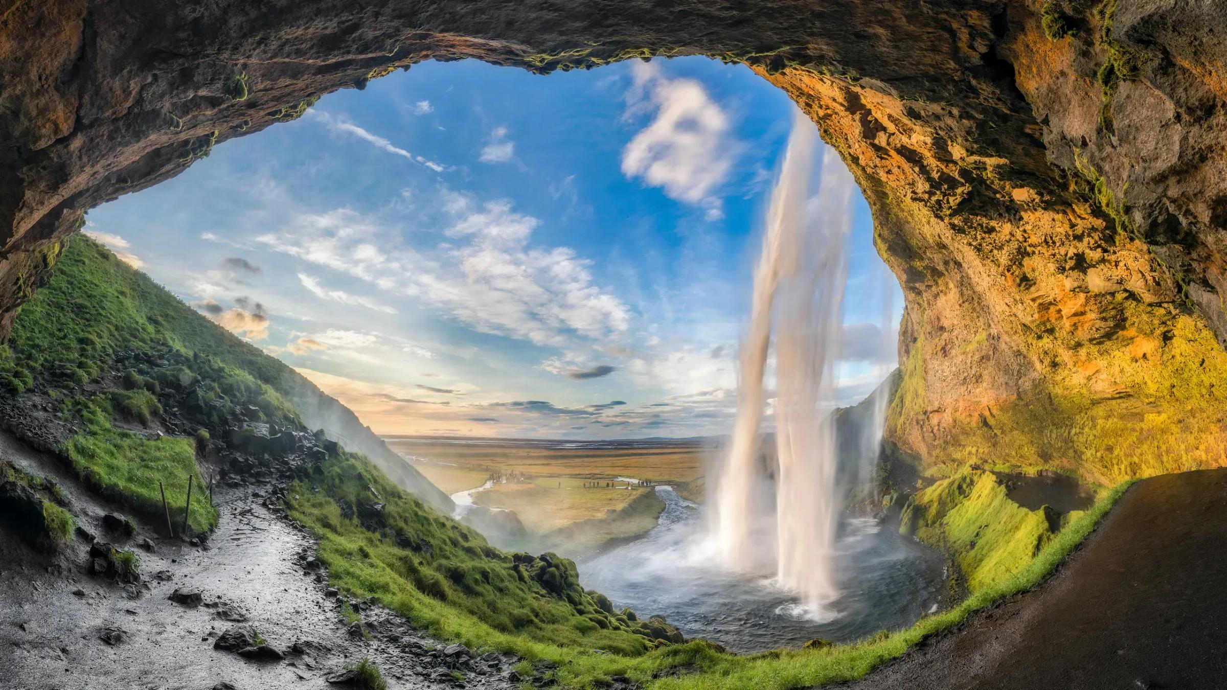 a waterfall is visible through the opening of a cave .
