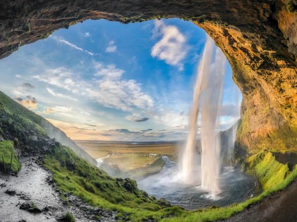 a waterfall is visible through the opening of a cave .
