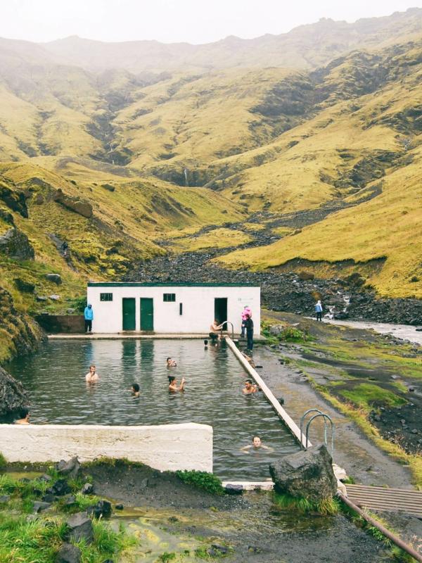 un grupo de personas está nadando en una piscina en medio de un valle montañoso.