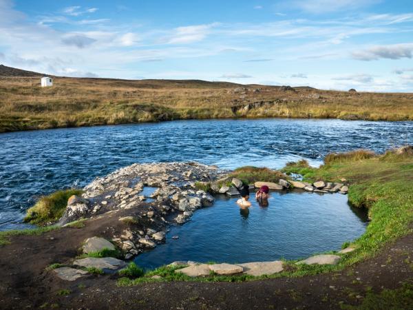 two people are swimming in a hot spring next to a river .