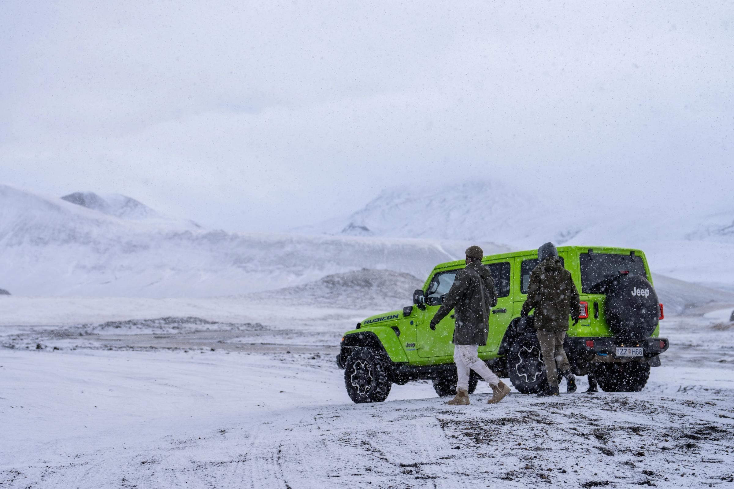 a group of people are standing next to a green jeep in the snow .