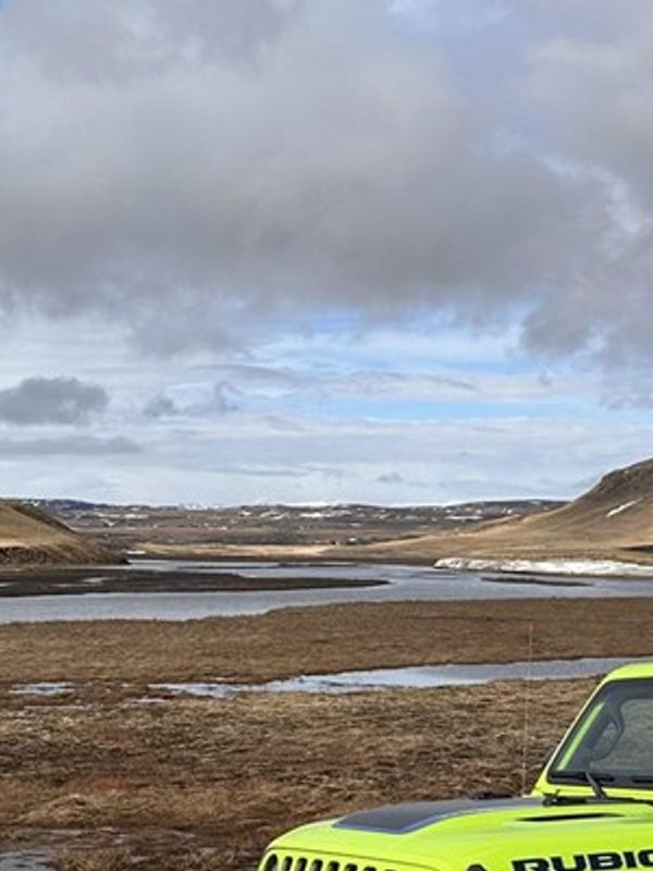a yellow jeep is parked in the middle of a field next to a body of water .