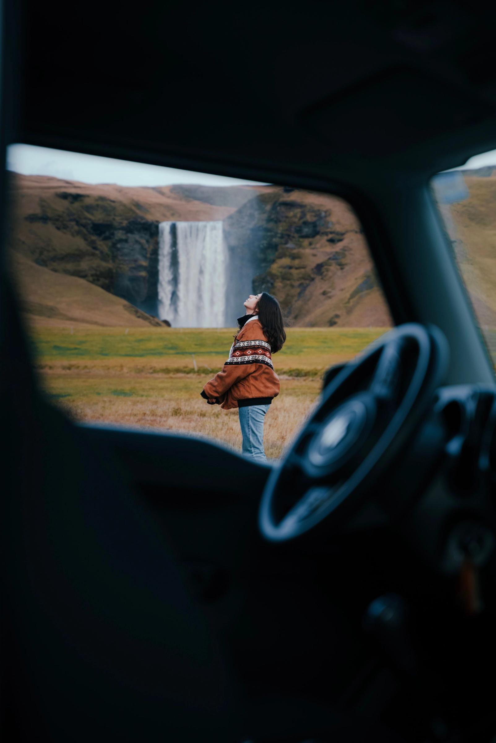 Mujer con su coche de alquiler en una cascada en Islandia