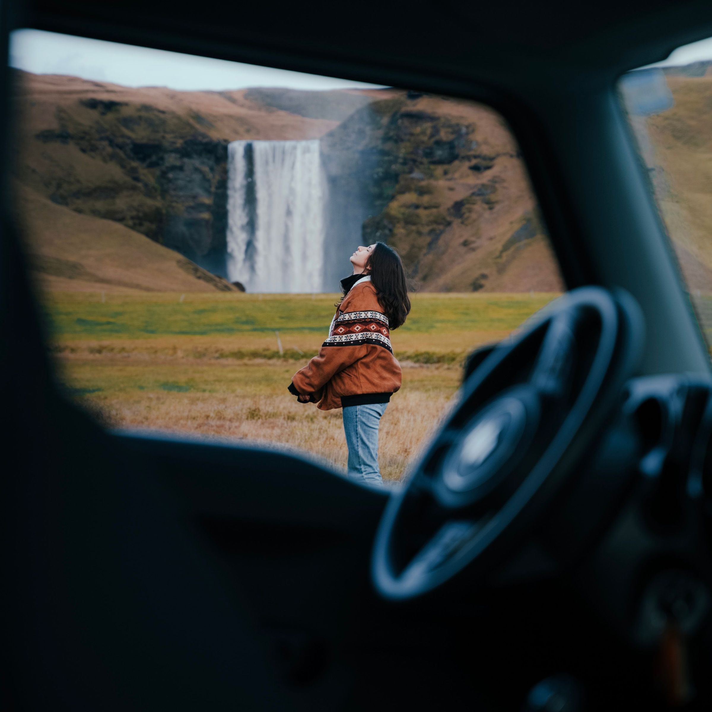 Mujer con su coche de alquiler en una cascada en Islandia
